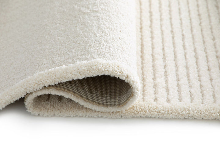 Rolled cream rug showing soft pile and backing.