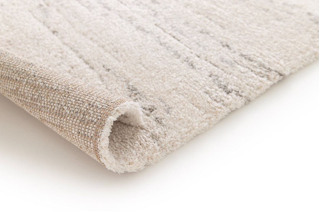 Rolled corner view of a cream rug with subtle grey streaks.