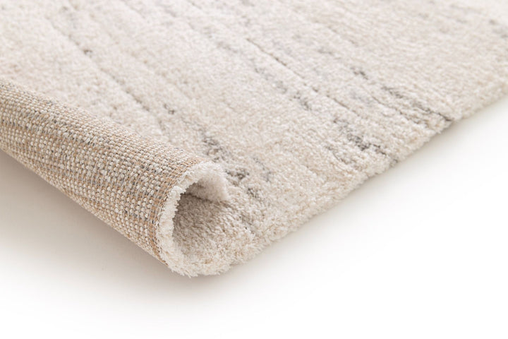 Rolled corner view of a cream rug with subtle grey streaks.