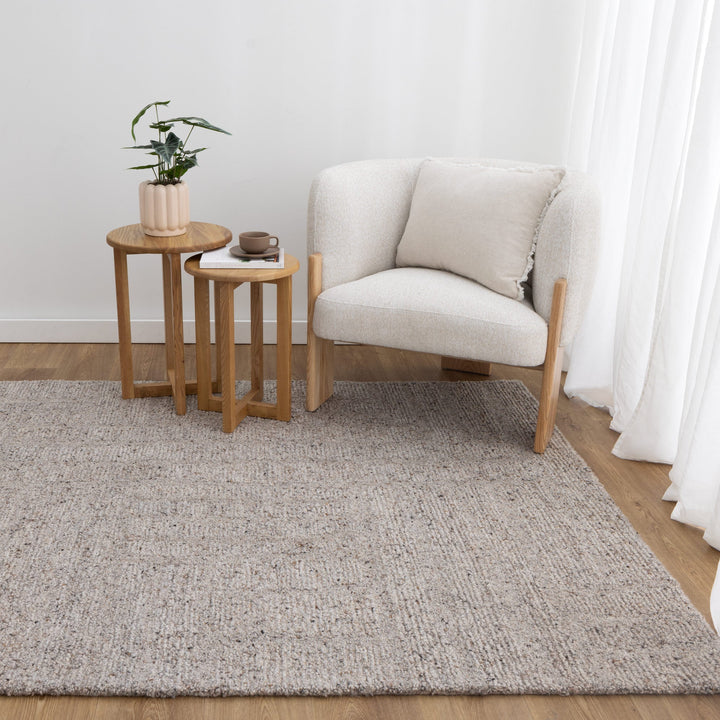 Light gray textured rug in a room with a white wall, wooden floor, and a light gray armchair.
