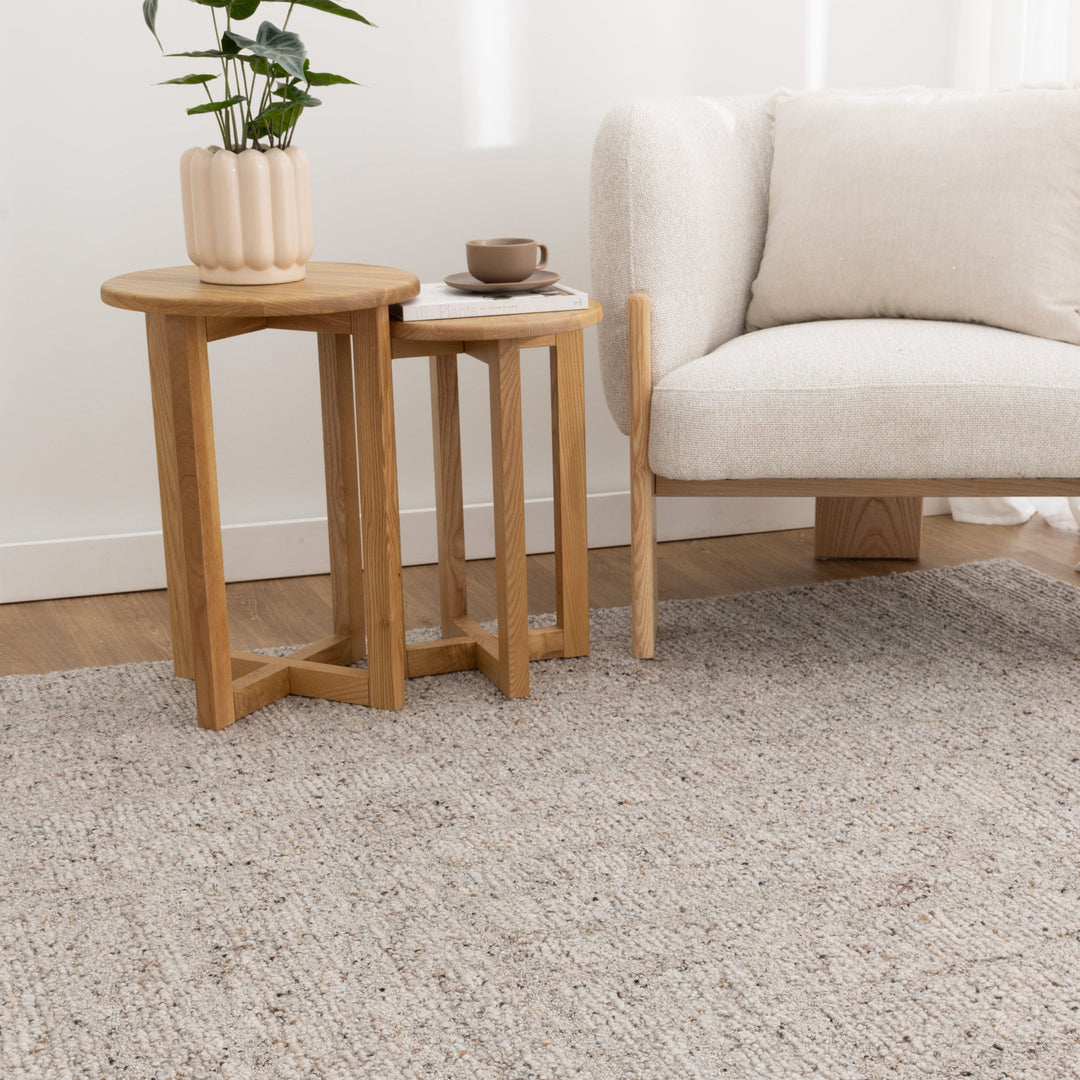 Two wooden side tables with a plant and bowl next to a beige sofa on a textured carpet.