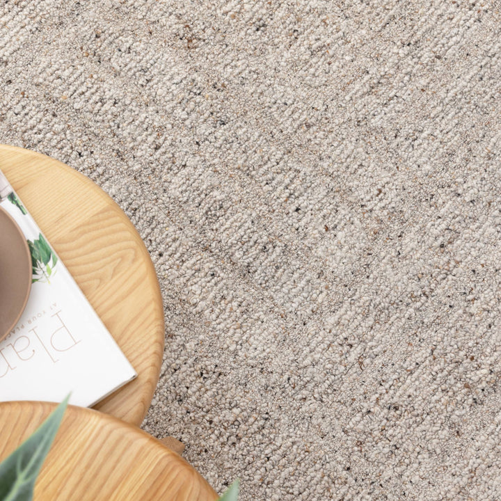 Close-up of a textured beige carpet with a wooden side table and plant in the foreground.