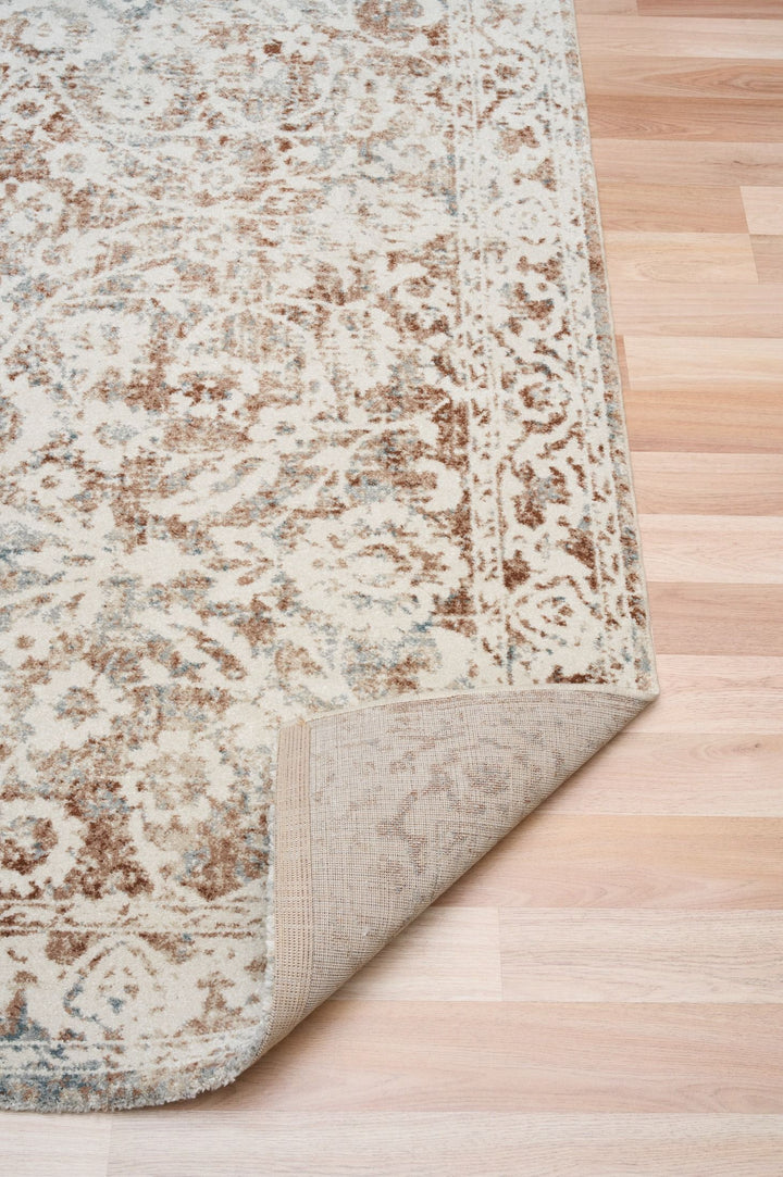 Curved corner view of a beige and brown floral rug.