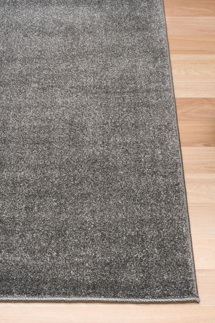 Close-up corner of a dark grey rug on wooden flooring.