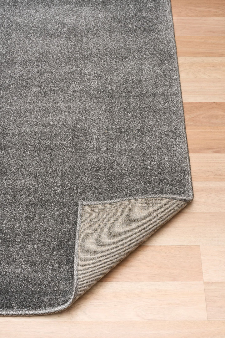 Dark grey rug corner lifted to show underside on wood floor.