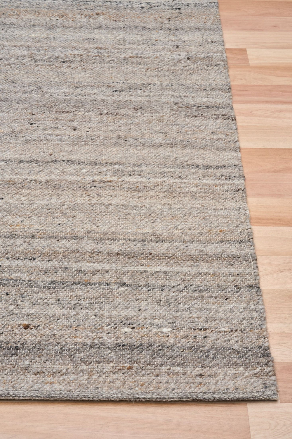 Angled close-up of dark grey rug corner on wooden floor.