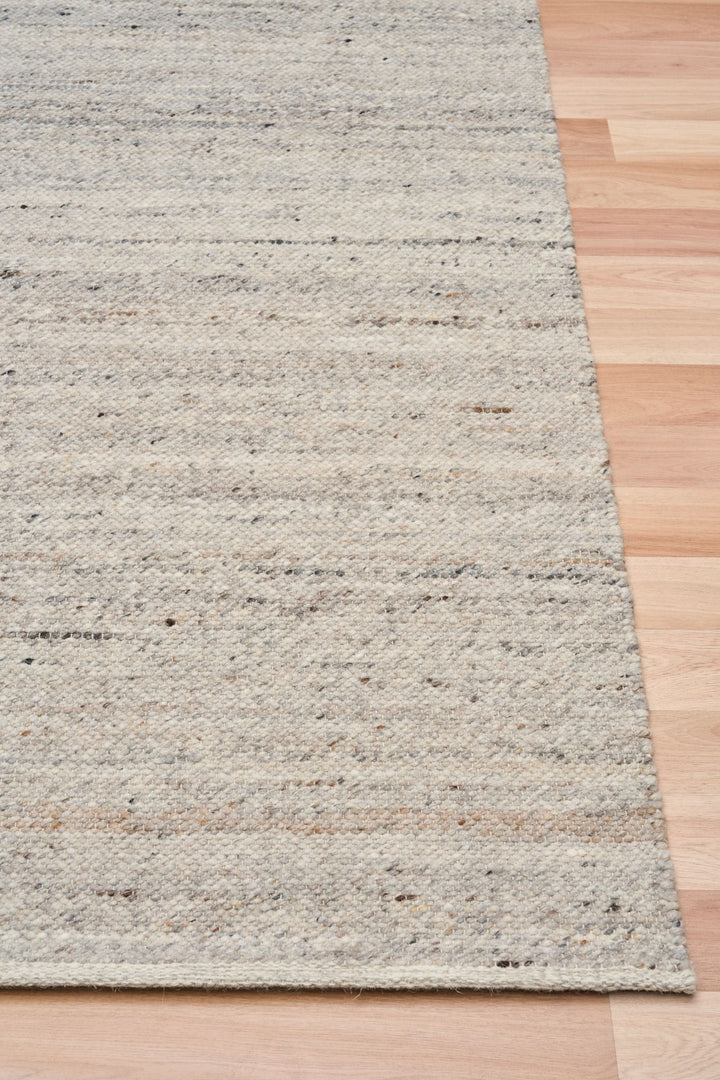 A close-up of the Harmony Smoke Grey rug corner on a wooden floor.