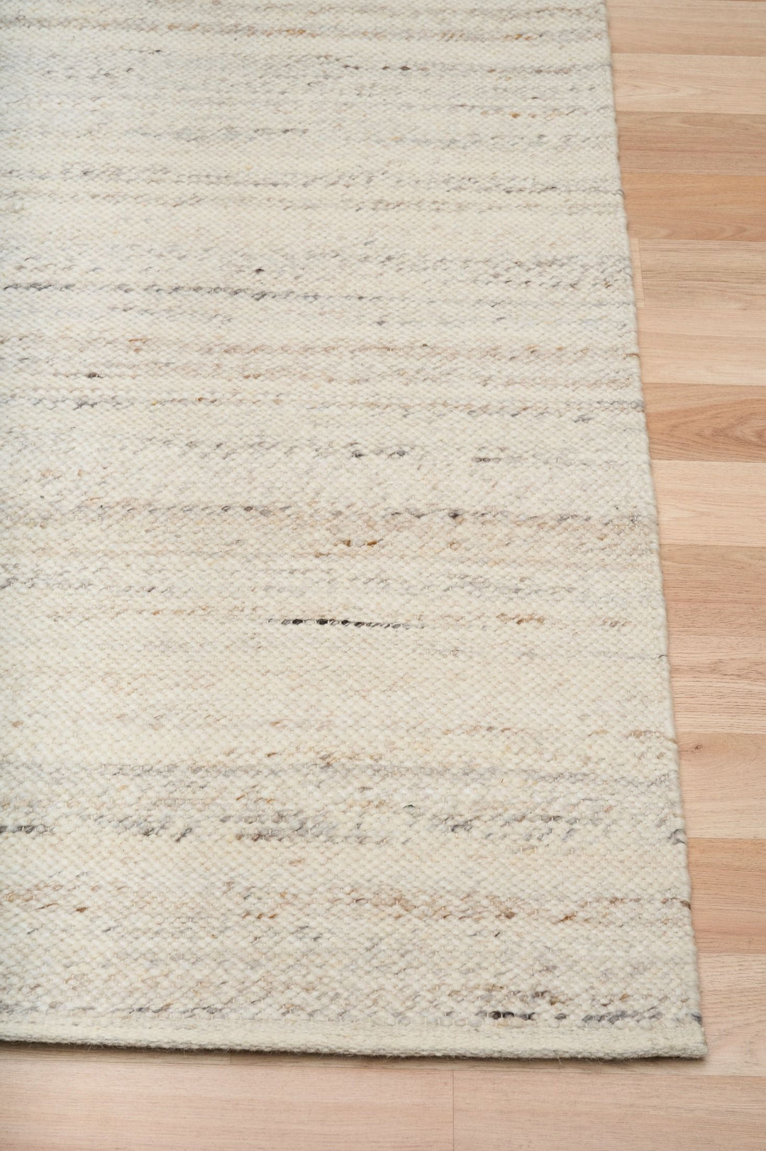 Close-up of a beige and ivory woven rug edge on a wooden floor.