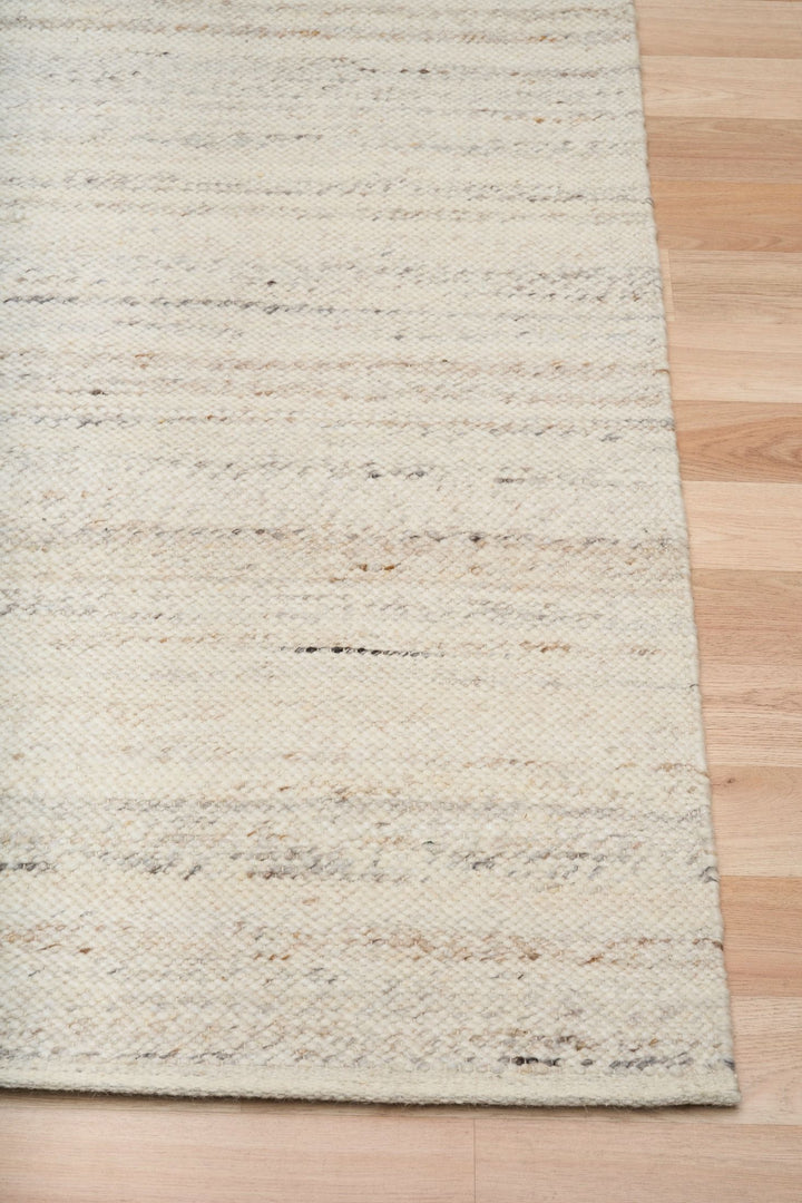 Close-up of a beige and ivory woven rug edge on a wooden floor.