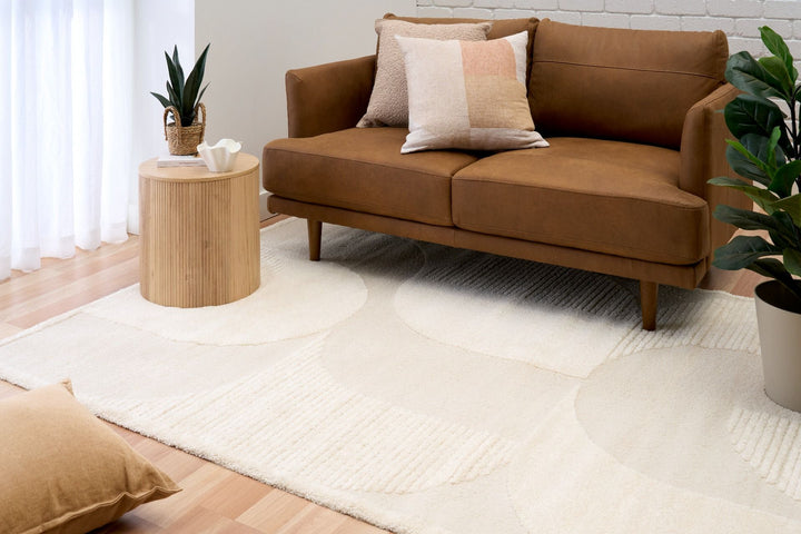 Cream rug styled in living room with brown sofa.