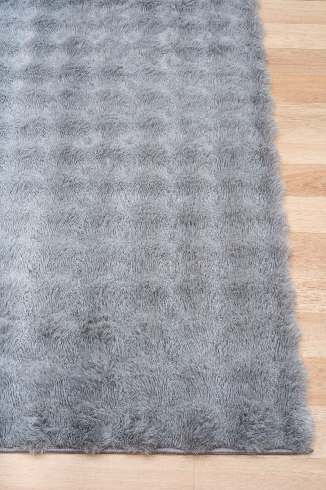 Close-up of light grey fluffy rug corner on wooden floor.