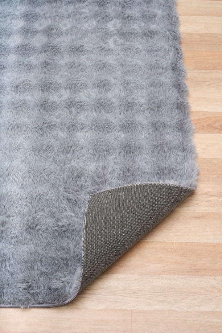 Close-up of light grey textured rug with corner flipped to show non-slip backing.