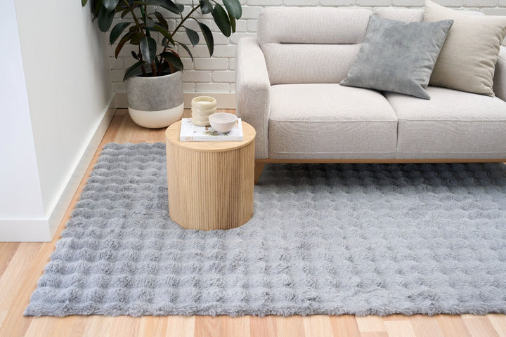 "Light grey textured rug in living room with beige sofa, cushions, and round wooden side table.