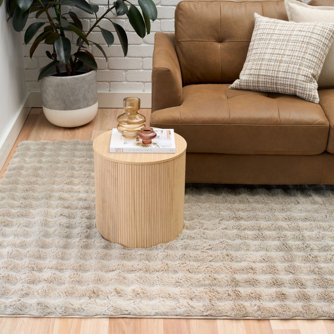 Modern living room with light beige textured rug, brown leather sofa, and round wooden side table.