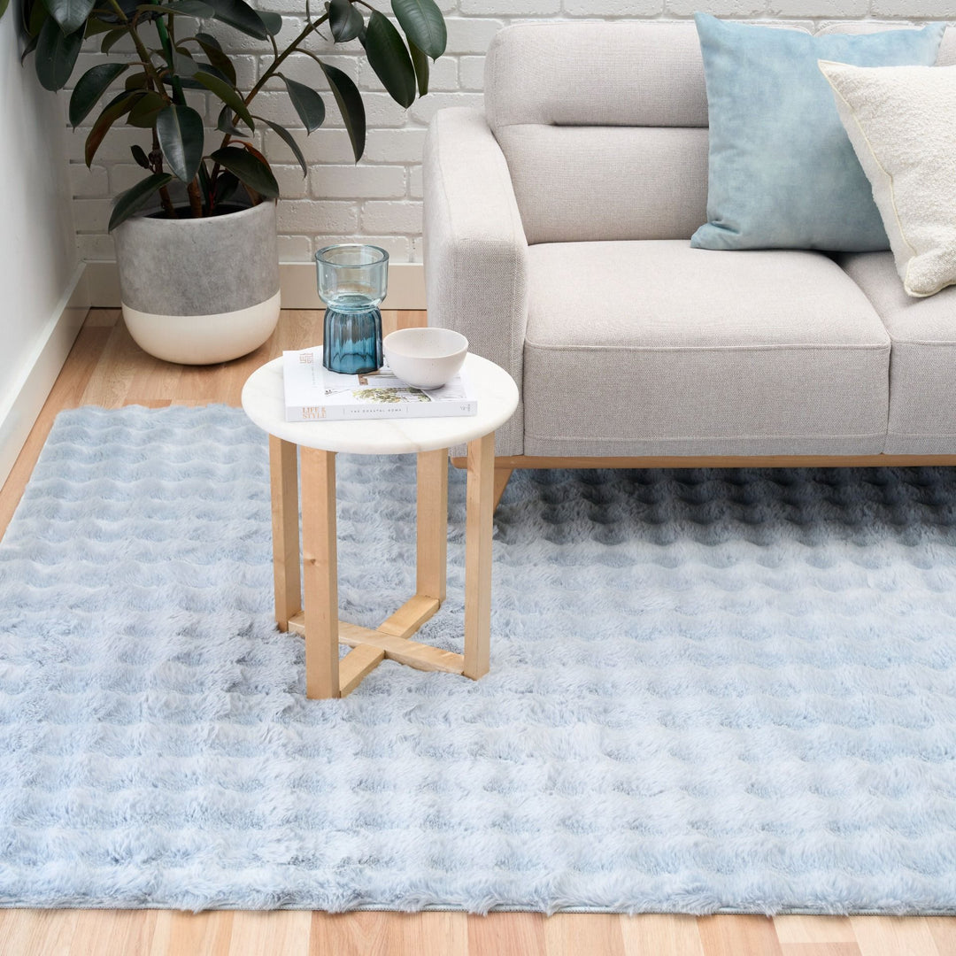 Modern living room with light blue textured rug, beige sofa, and small round side table.