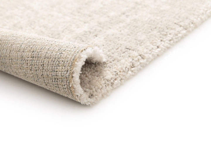 Close-up of a rug corner rolled to show the backing.