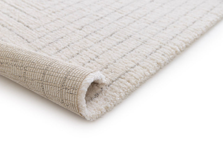 Close-up of a cream rug corner showing woven backing and soft pile.