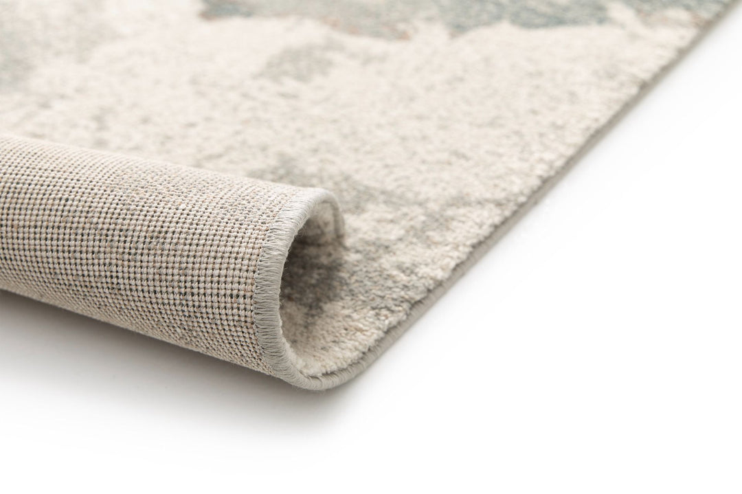 A close-up of a rug corner curled upward to show the weave backing.