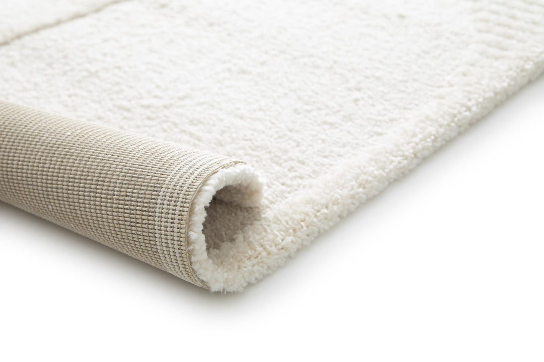 Close-up of a cream rug corner rolled to show the backing.