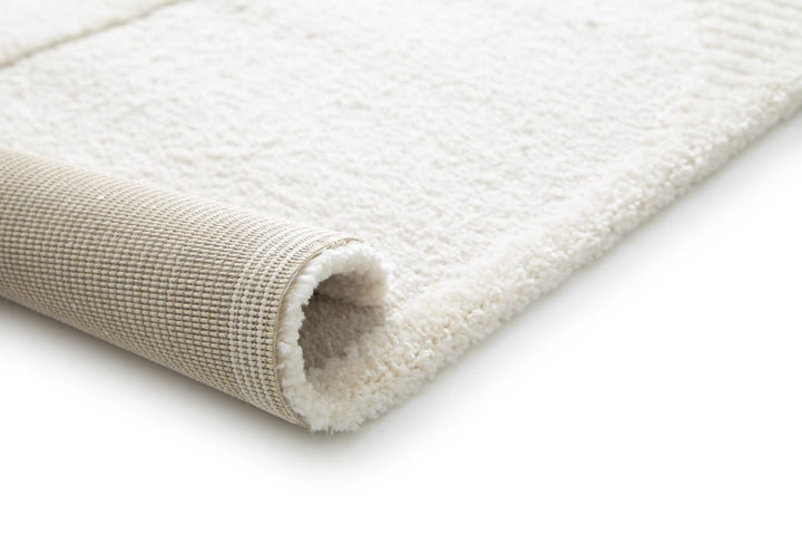 Close-up of a cream rug corner rolled to show the backing.