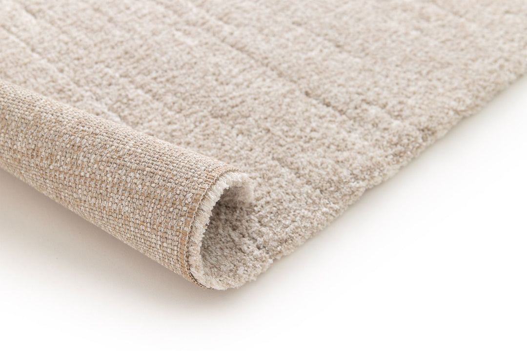 Rolled corner view of a soft beige rug.