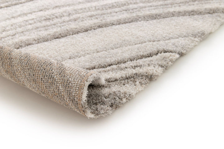 Rolled corner view of grey and cream rug with wave pattern.