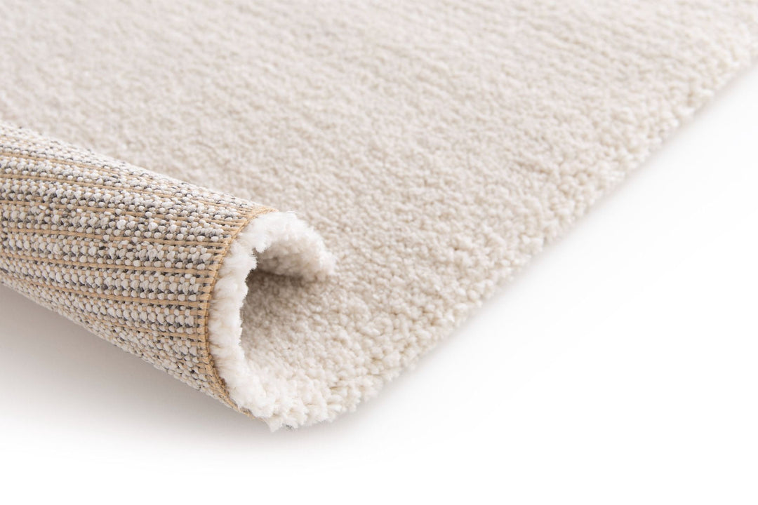 Rolled corner of beige rug showing backing weave and pile.