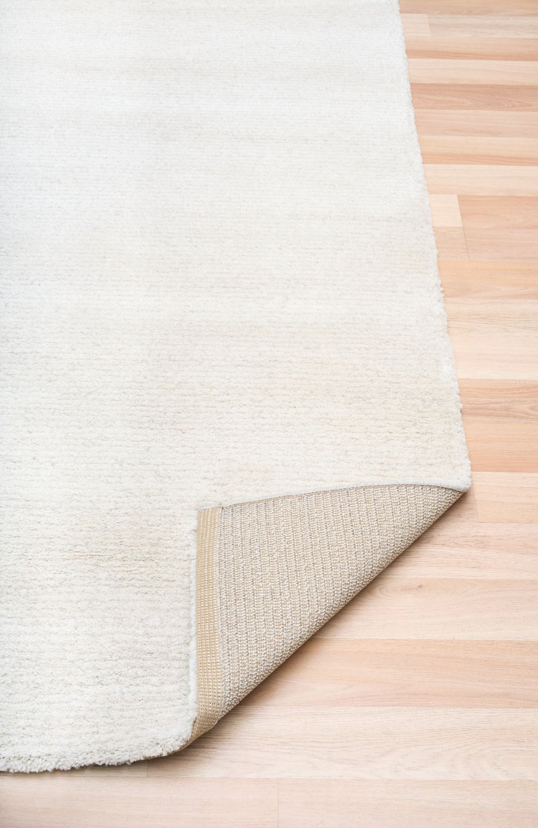 White rug with a corner lifted to show the woven underside.