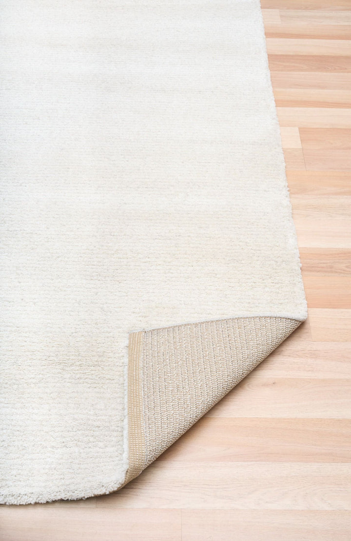 White rug with a corner lifted to show the woven underside.