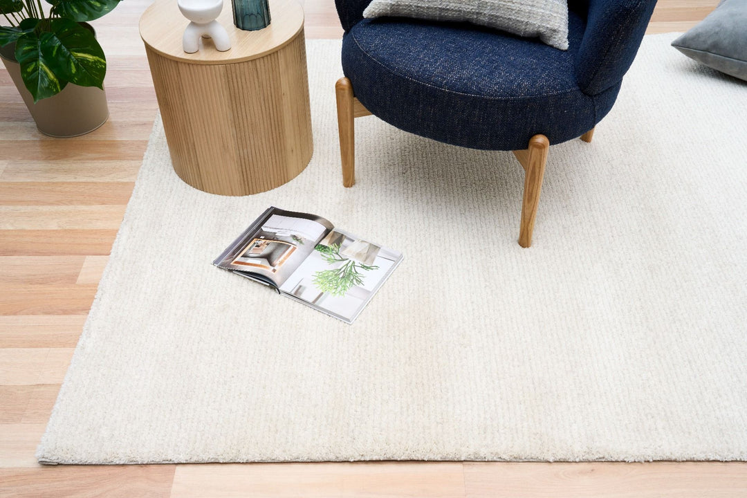 White rug under a chair and table with an open magazine on top.