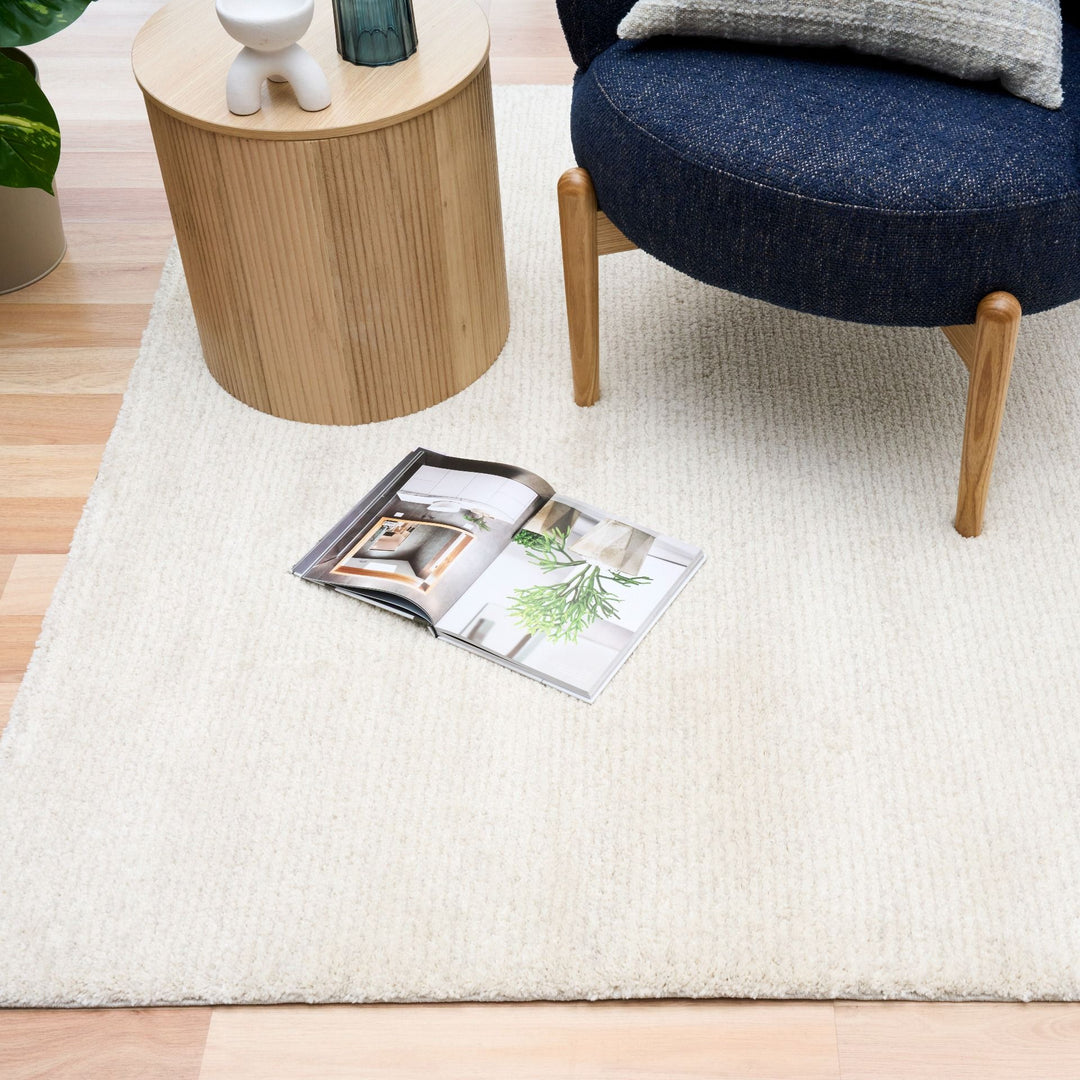 White rug in a living room with a blue chair, side table, and open magazine.