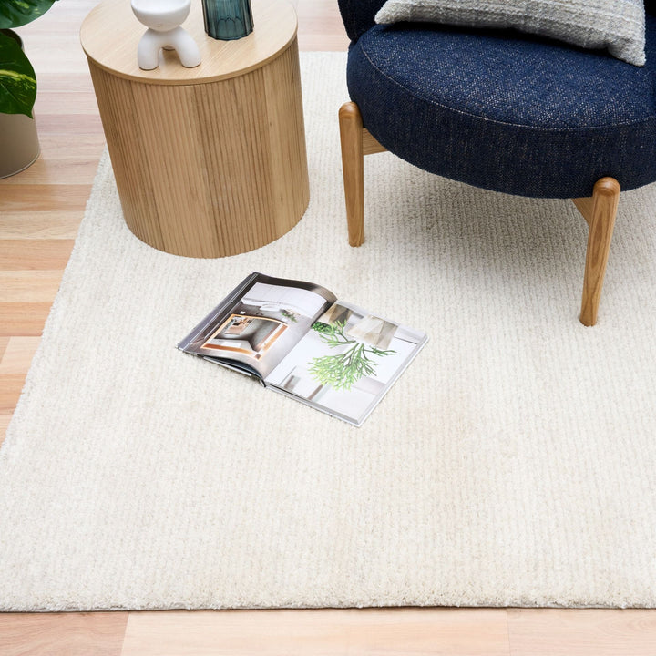 White rug in a living room with a blue chair, side table, and open magazine.