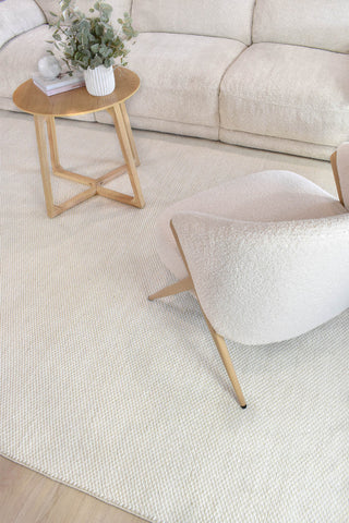 Light-colored rug in a living room with a sofa, side table, and chair.