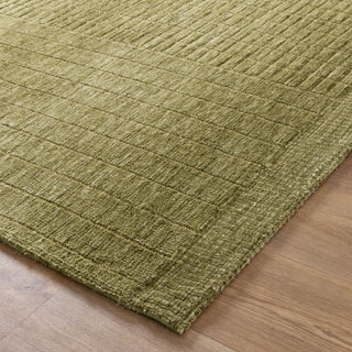 Corner view of olive green rug on a wooden floor.