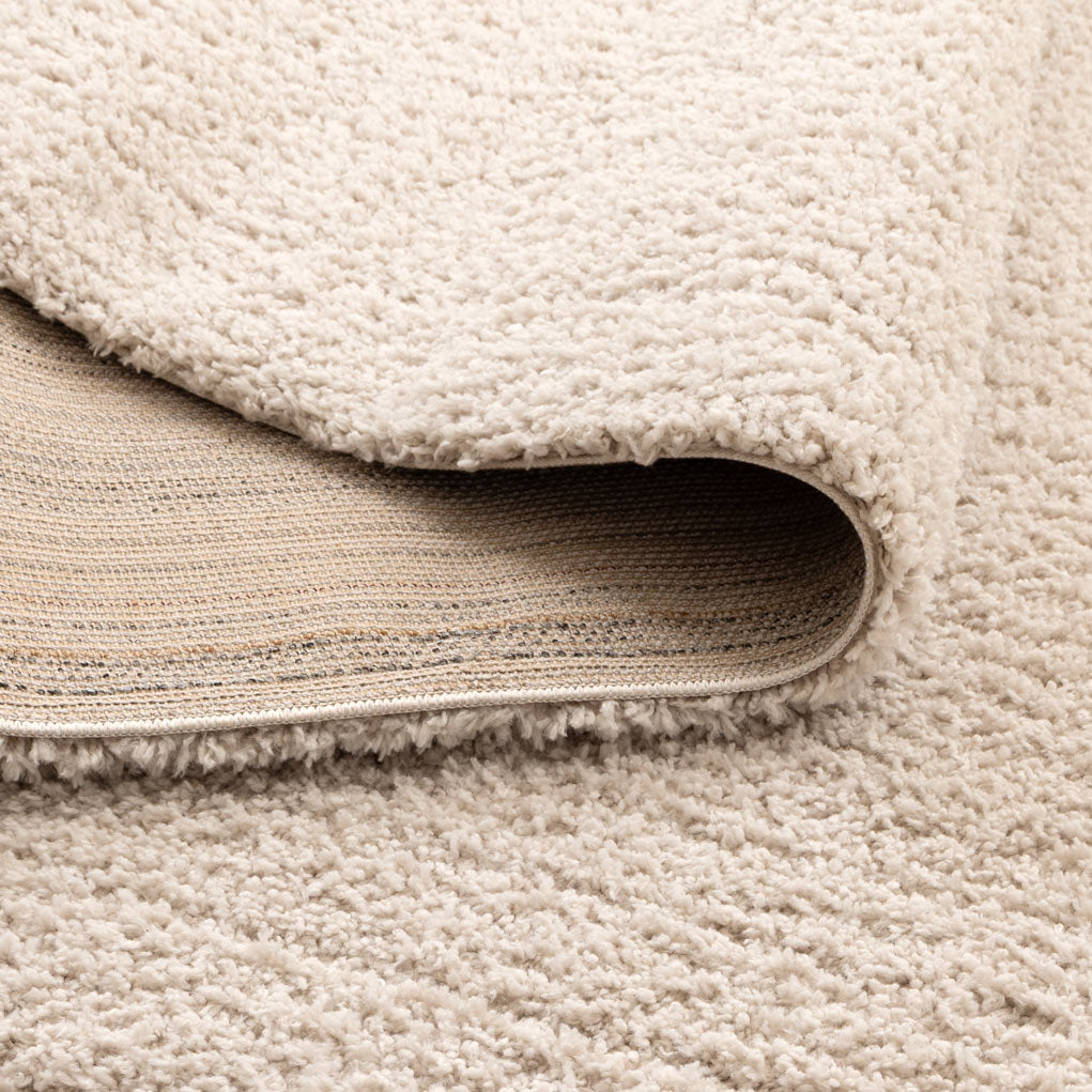 Close-up of a textured area rug in a warm cream or off-white color, with one corner folded over to show the backing.