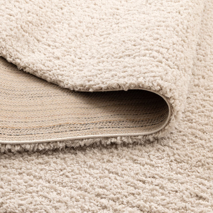 Close-up of a textured area rug in a warm cream or off-white color, with one corner folded over to show the backing.
