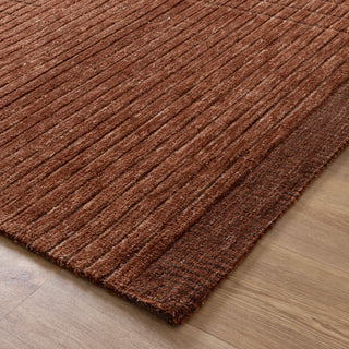 Corner close-up of terracotta textured rug placed on wooden flooring.