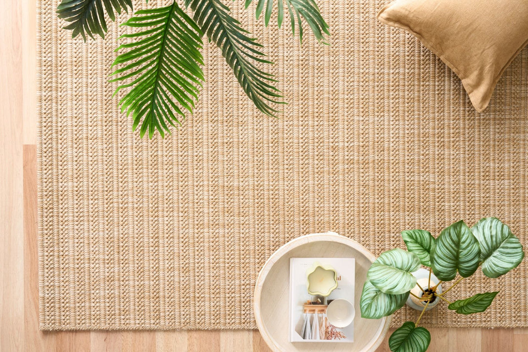 Beige ribbed rug on wood floor with palm fronds, throw, and tray.