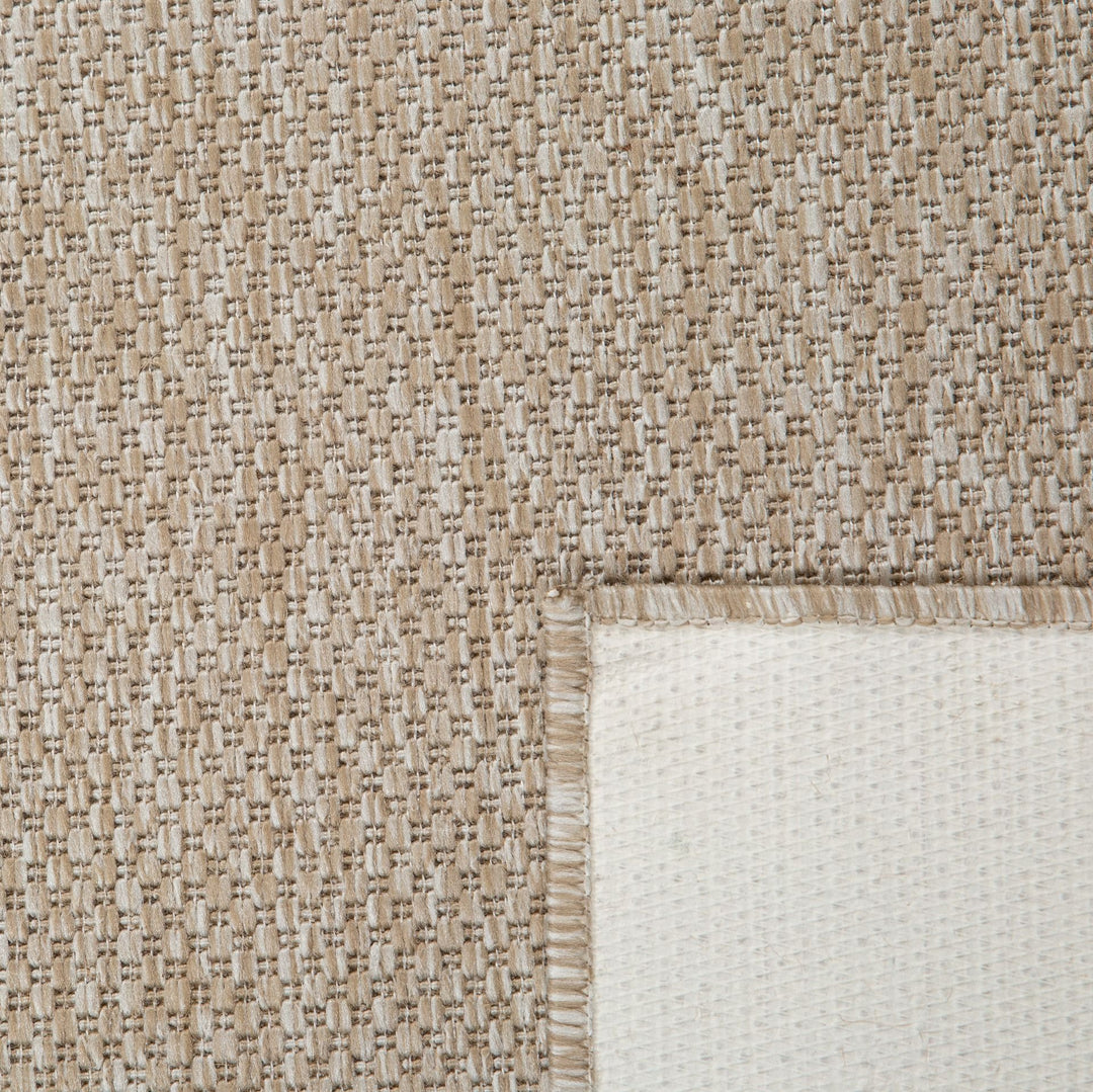 Corner close-up of sand rug with white backing.