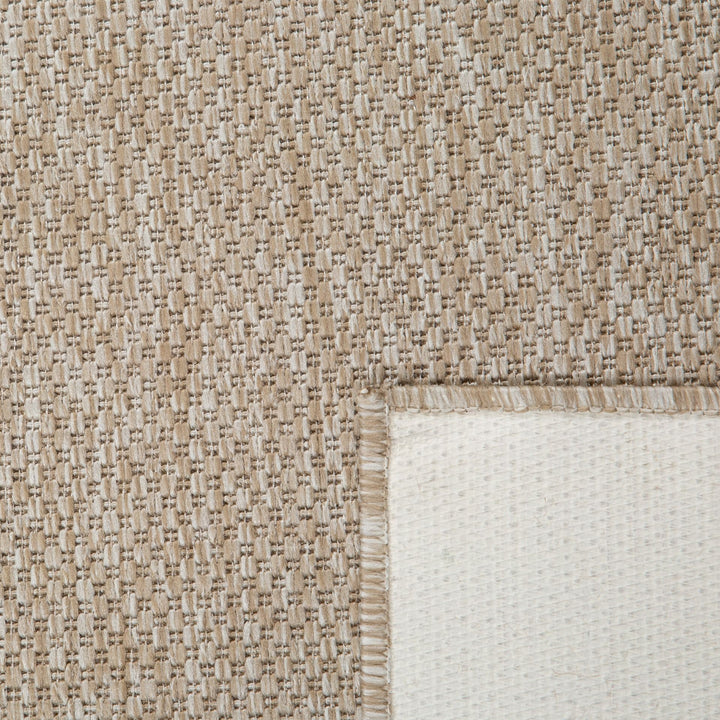 Corner close-up of sand rug with white backing.