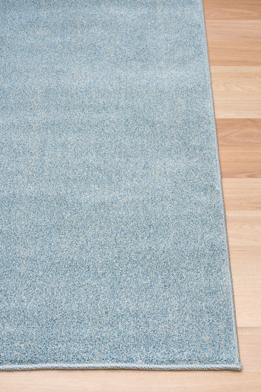 Close-up of the light blue rug corner placed on a wooden floor.