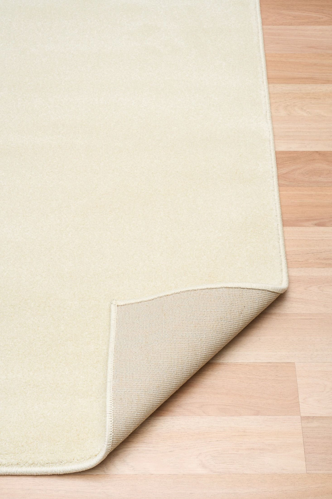 Cream-colored rug with folded corner showing underside backing.