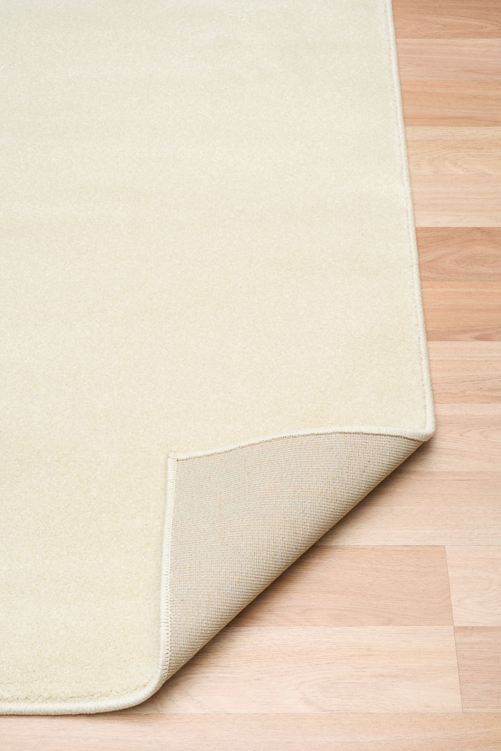 Cream-colored rug with folded corner showing underside backing.