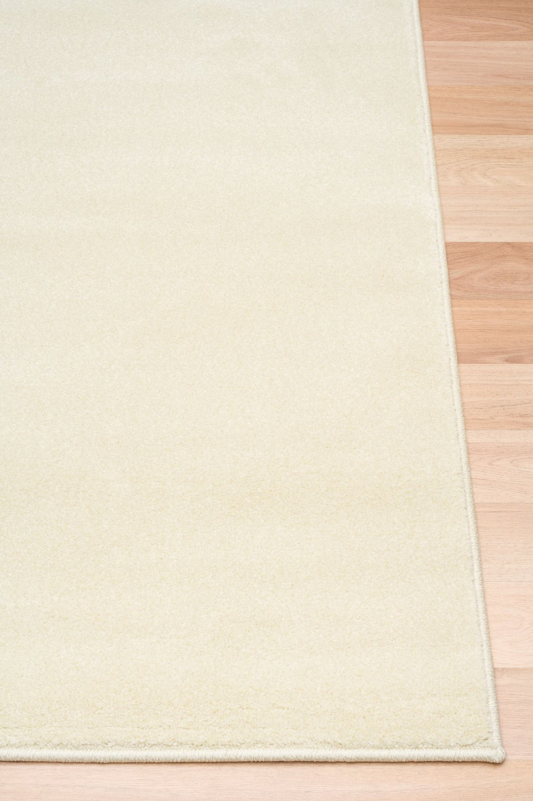 Close-up of a cream-colored rug corner placed on wooden flooring.