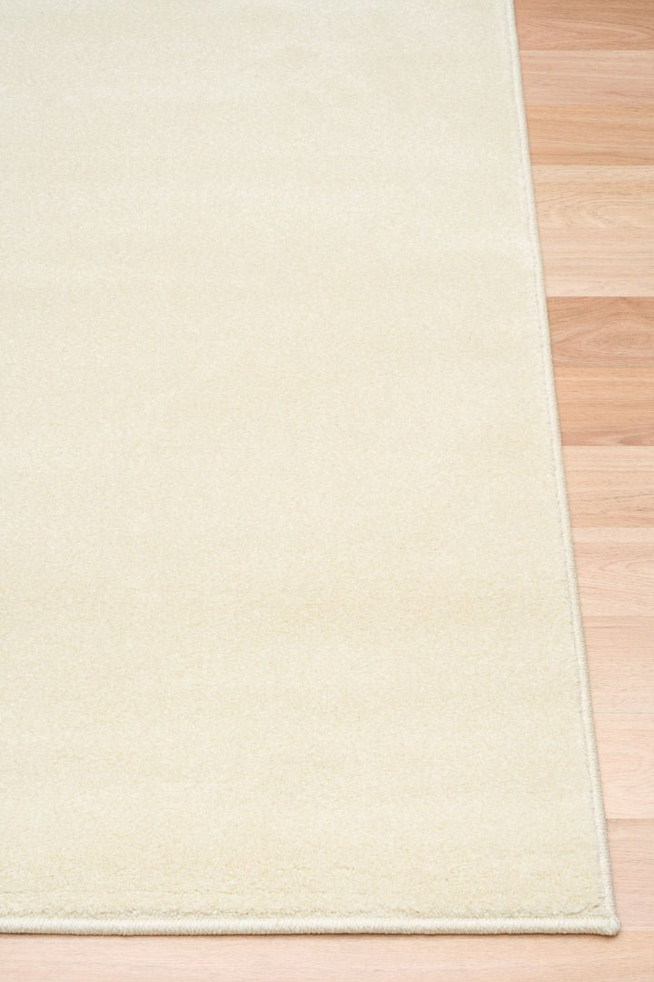 Close-up of a cream-colored rug corner placed on wooden flooring.