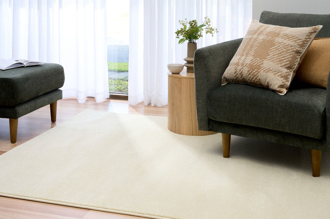 Living room with a cream rug under a dark green sofa and cushions.
