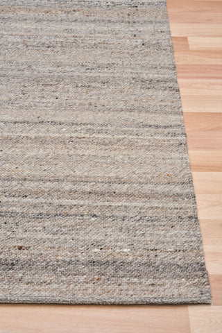 Angled close-up of dark grey rug corner on wooden floor.