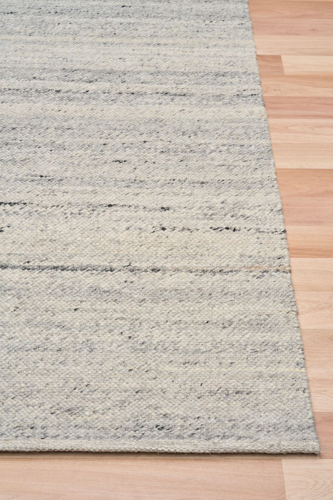 Close-up of silver rug corner on wooden floor showing texture.