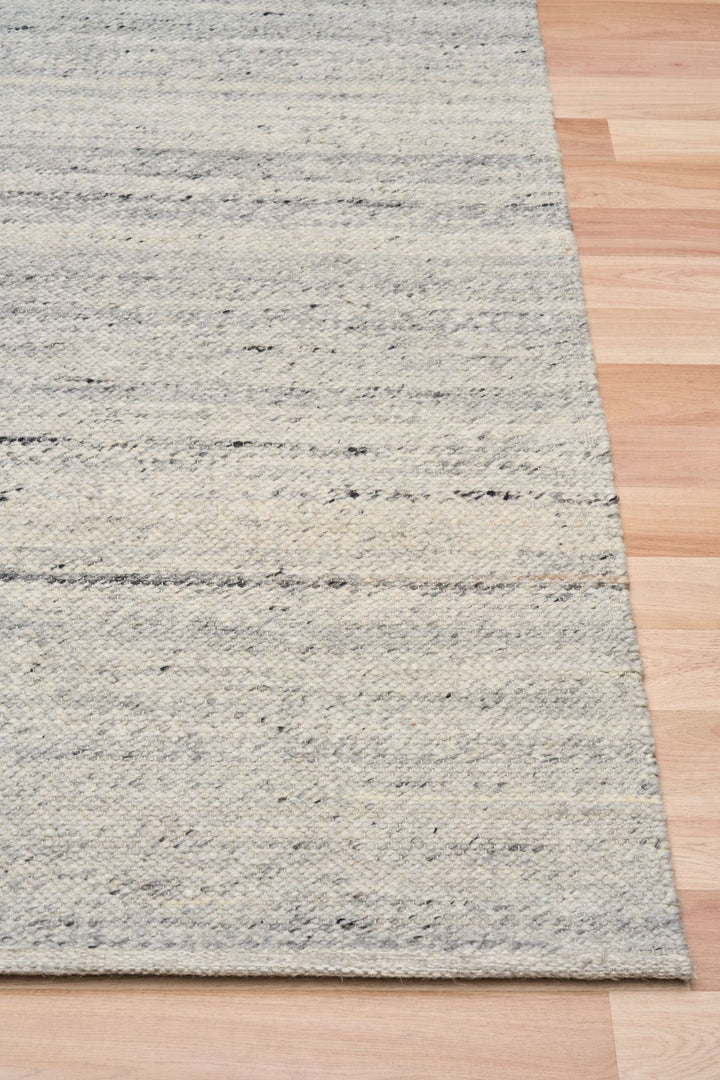 Close-up of silver rug corner on wooden floor showing texture.