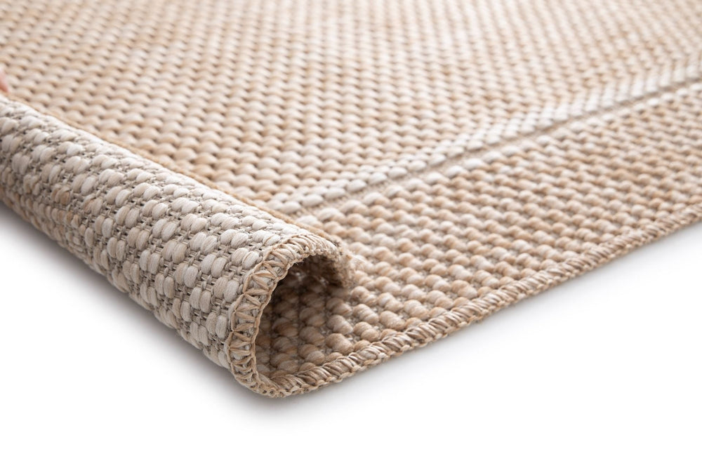 Close-up of Barton 41505/70 area rug in warm beige, basket-weave texture, edge stitched, with a rolled corner showing the backing on a white background.